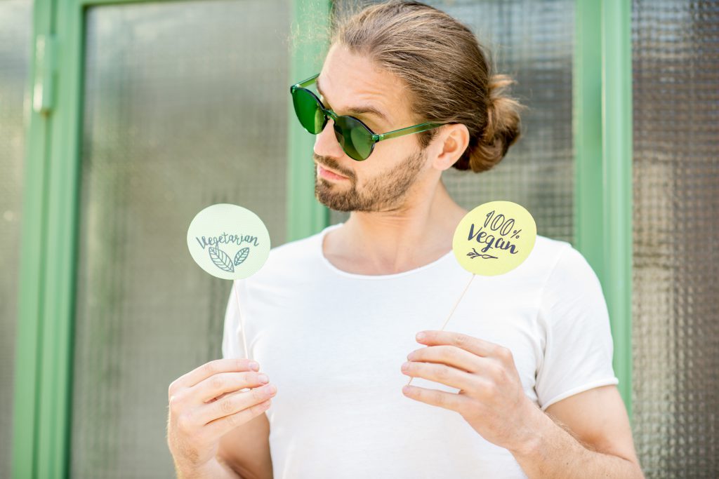 Handsome man holding green plates with healthy eating slogans outdoors on the green background