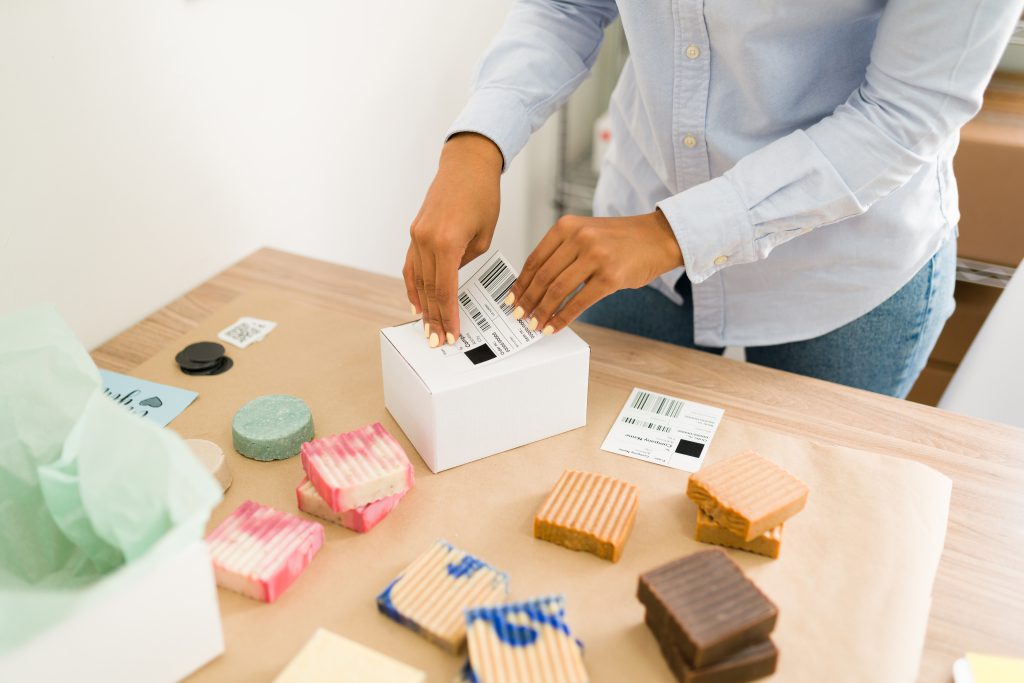 Close up of female hands putting a shipping label on a package with beauty natural products and arranging online customers' orders